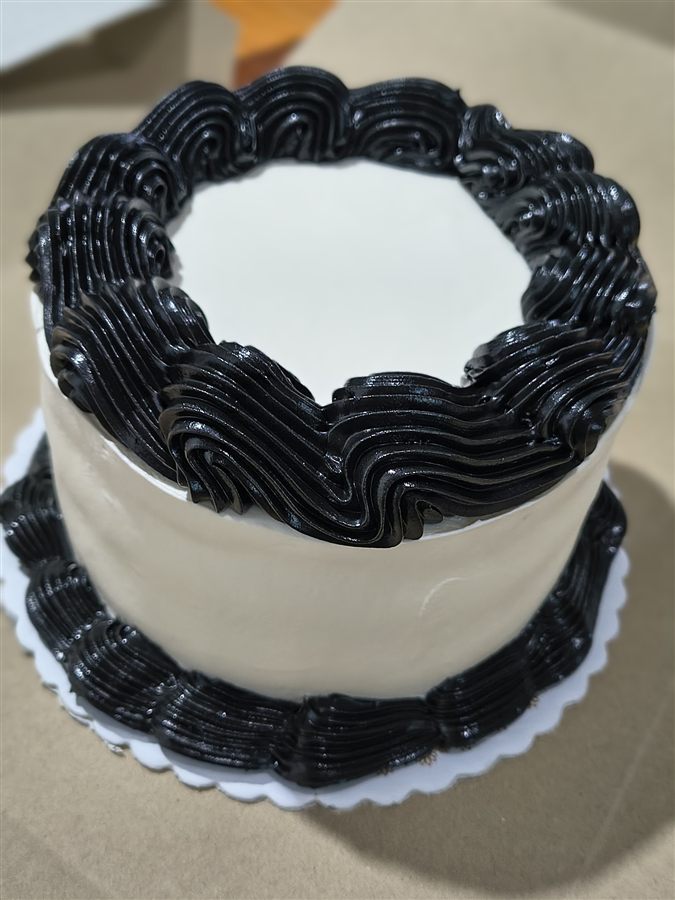Torta de terminación minimalista, con hilo de chocolate negro cayendo por el borde, sobre un plato blanco.