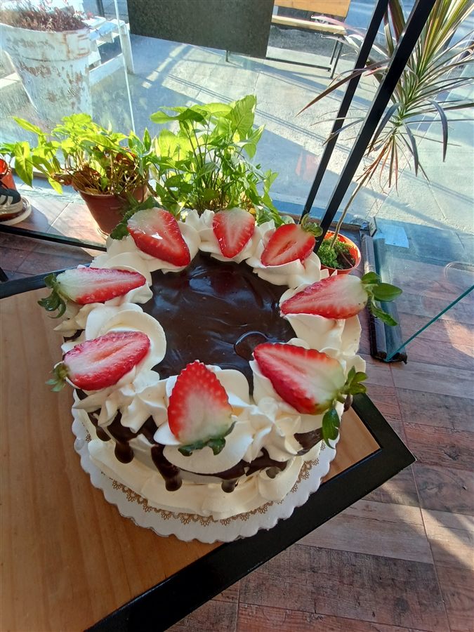 Torta de chocolate con frutillas frescas; detrás, la ventana y la calle.