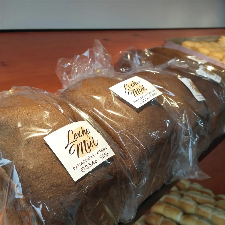 Panes envueltos en la estantería, cada uno con la etiqueta de Leche & Miel, y una canasta de facturas detrás.