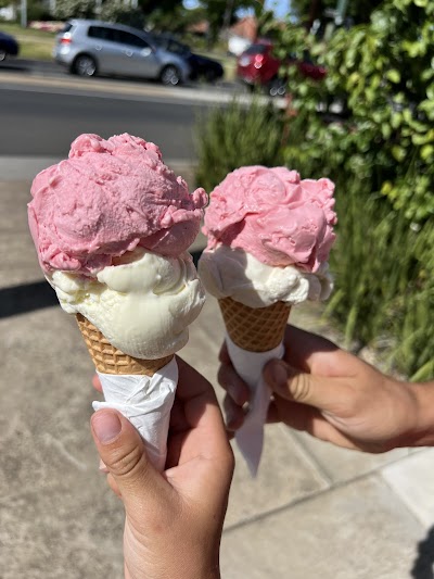 A hand holding a double-scoop gelato cone in sunshine outside Favourite Flavours