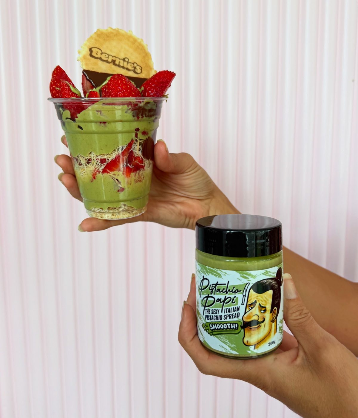 A pistachio gelato parfait cup topped with strawberries and a Bernie's wafer