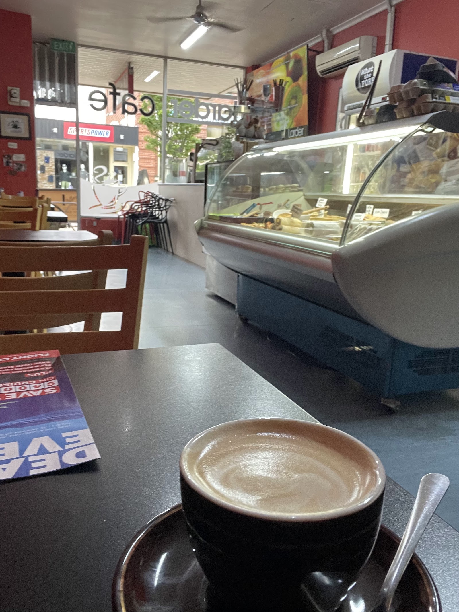 Inside The Larder Cafe — warm red walls, timber seating and the deli cabinet