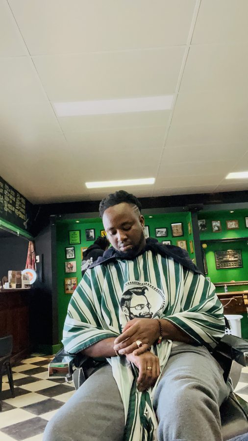 A customer mid-service in the chair inside Ross C's, with the shop's green walls and framed photos behind