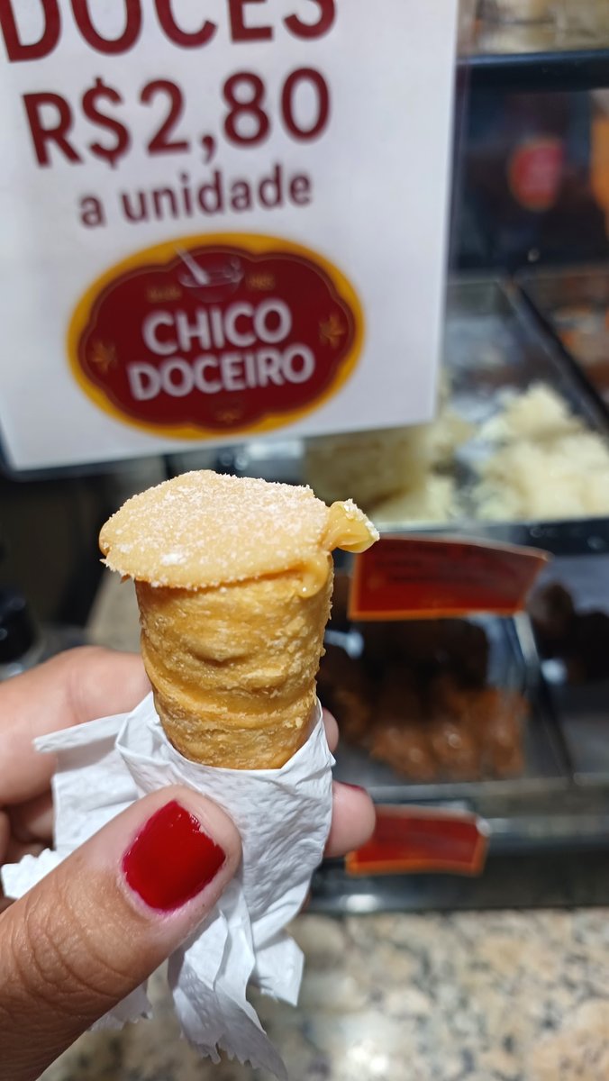 Canudinho de doce de leite recém-feito, segurado à frente da placa da Chico Doceiro
