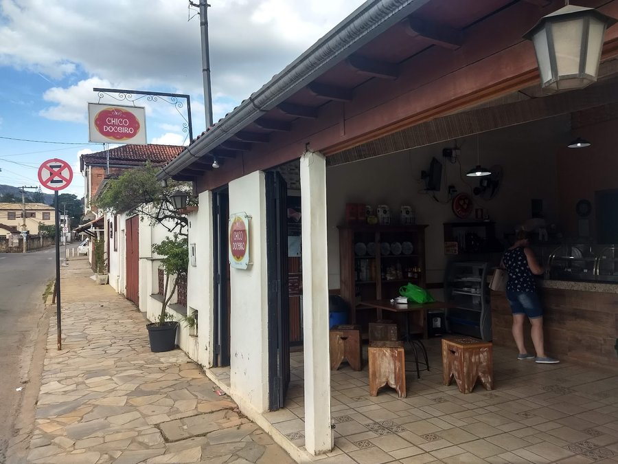 Fachada colonial da Chico Doceiro em Tiradentes, com a placa suspensa e um cliente no balcão