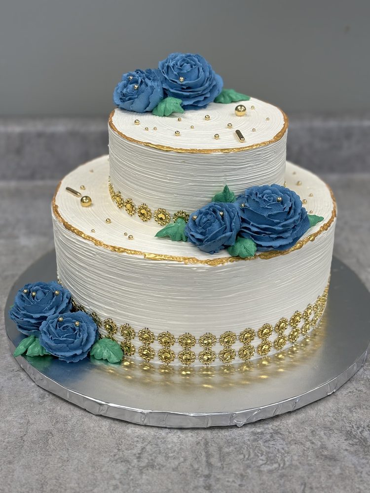 Two-tier celebration cake with blue buttercream roses and gold accents