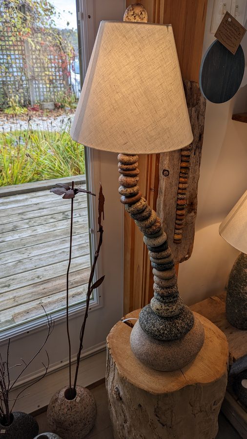 A handmade lamp of stacked beach stones on a driftwood base