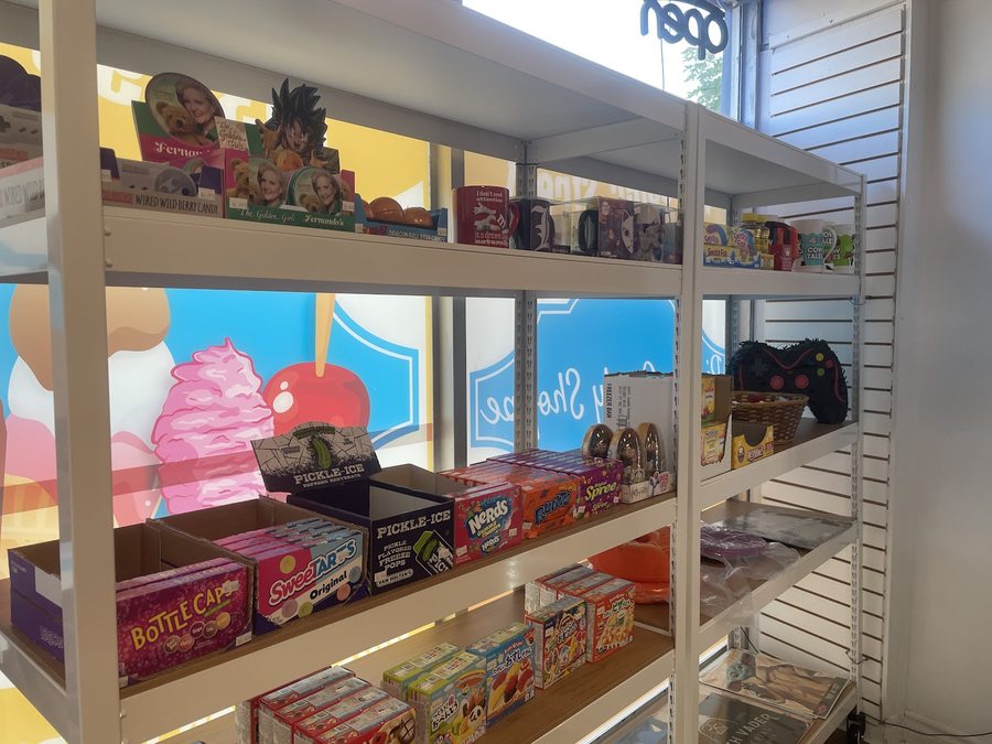 A shelf of retro and novelty candy — collector tins, boxed sweets, freezer pops and mugs — with the shop's window decal behind.
