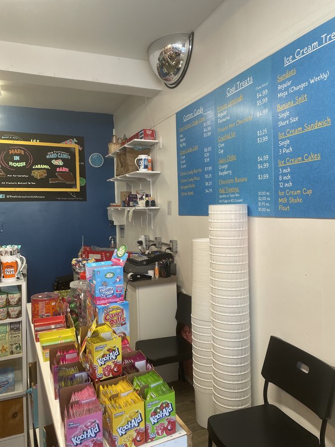A chalkboard headed MADE IN HOUSE beside the shop counter, listing fudge, caramel, marshmallows, hard candy and bark, below the blue-and-gold ice cream price board.