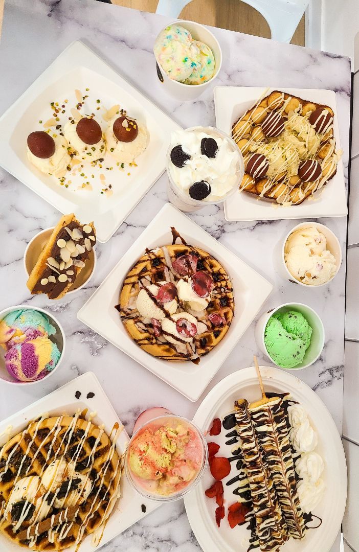 A spread of The Chill Desire desserts: a loaded round waffle, colourful ice-cream cups and milkshakes on a marble table