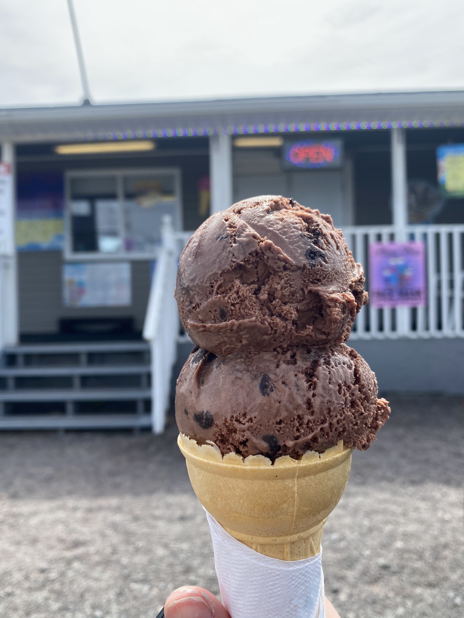 A generous double-scoop chocolate-chip cone held in front of Corina's Ice Cream Parlour