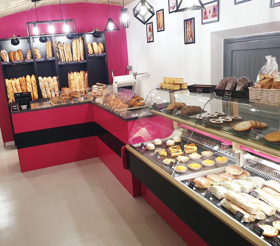 Inside Boulangerie du Moutas — bread wall, glass pastry case, and counter