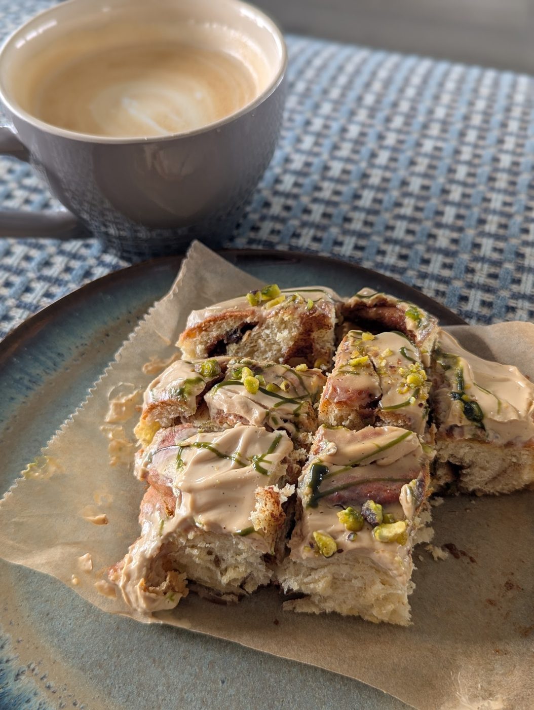 Pistachio babka square with a glossy glaze, served beside a flat white