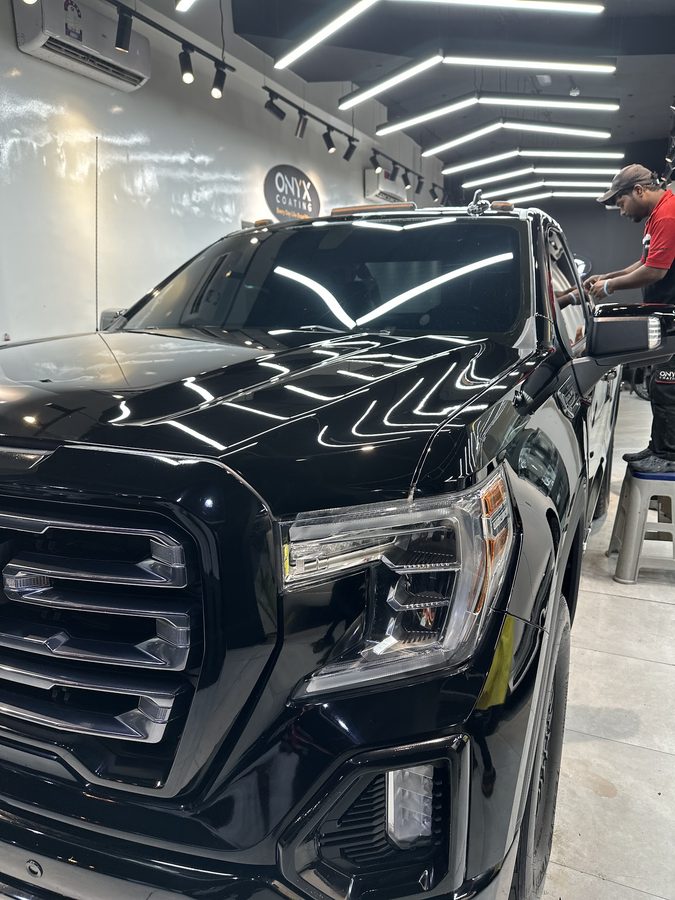 Close-up of a black vehicle hood with a swirl-free, mirror-like finish under showroom lighting.