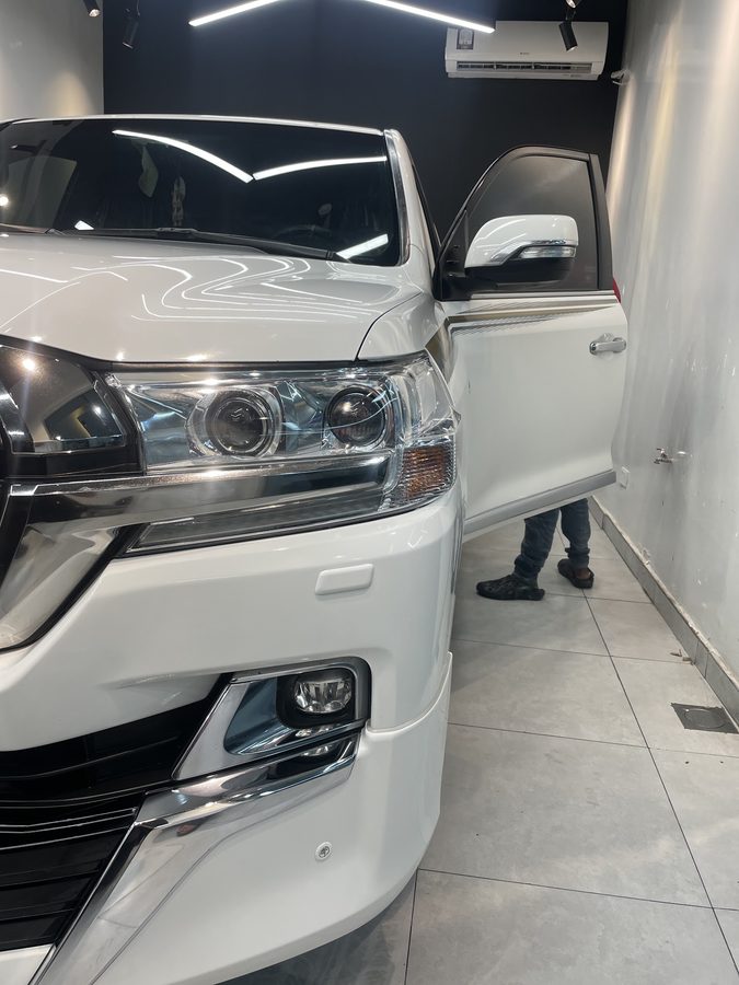 Technician fitting clear paint protection film along a white SUV door edge.