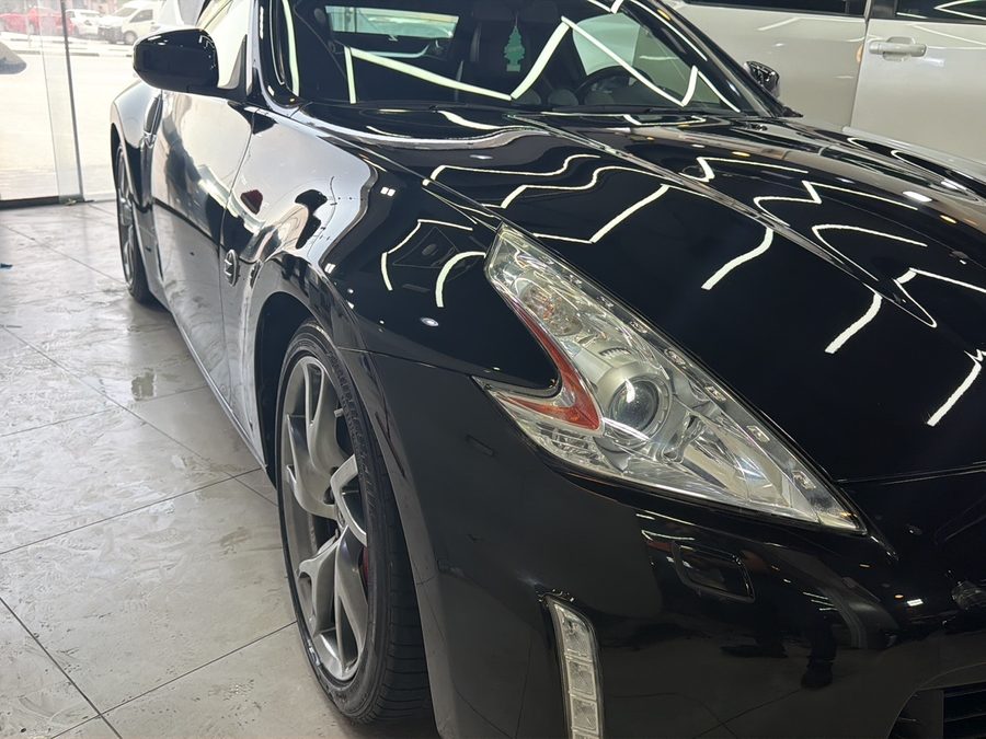 Close-up of a black coupe fender and headlight with a high-gloss polished finish.