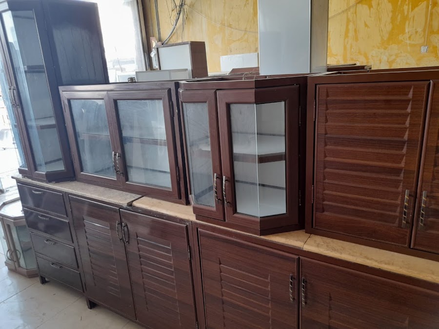 دواليب بدرف شيش بلون الجوز ووحدات علوية زجاجية بزوايا مشطوفة فوق سطح رخامي فاتح
