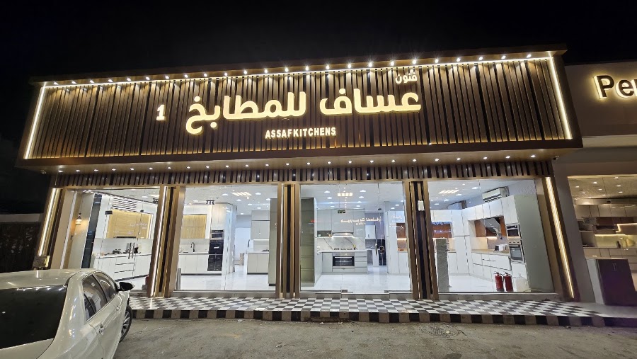 واجهة معرض عساف للمطابخ ليلًا بألواح خشبية مضاءة واسم المحل بالعربي