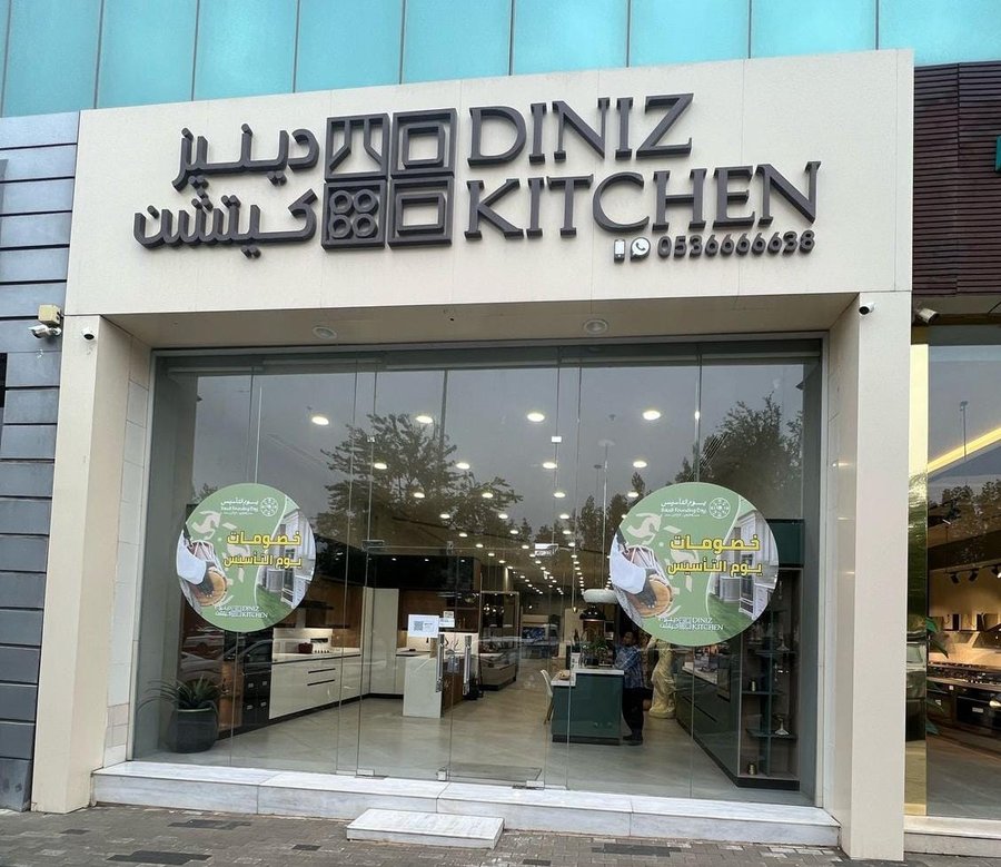 واجهة معرض دينيز كيتشن: لافتة بالعربية والإنجليزية فوق واجهة زجاجية يظهر خلفها معرض مضاء