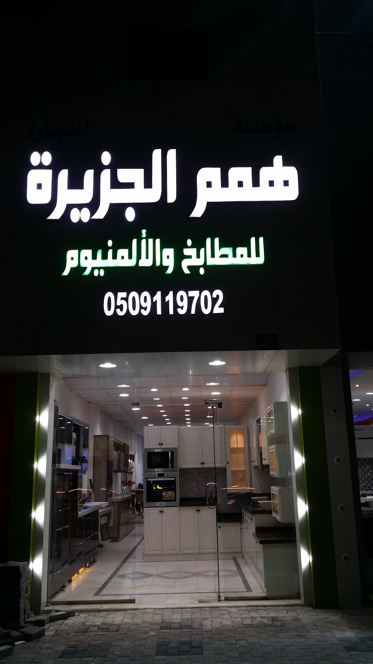 واجهة معرض همم الجزيرة ليلاً بلوحتها المضيئة وممر الإنارة إلى الداخل