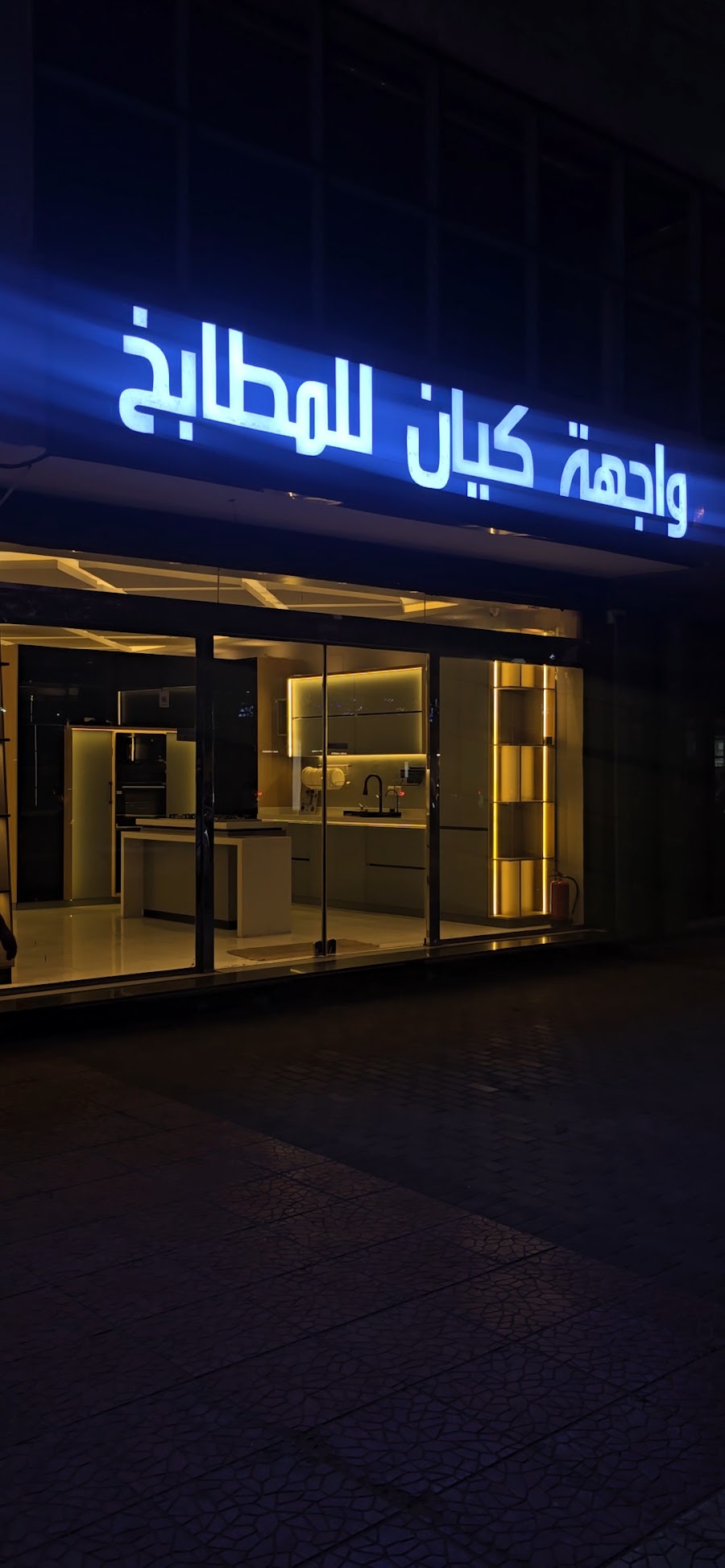 المعرض في المساء، اللوحة مضاءة والمطابخ المضاءة ظاهرة من خلف الزجاج