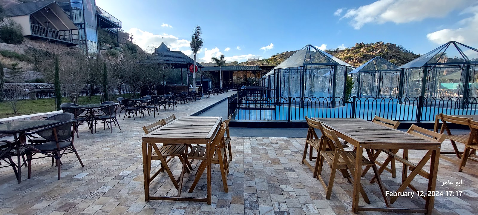 Wooden dining terrace with glass gazebos and mountain backdrop at Baz