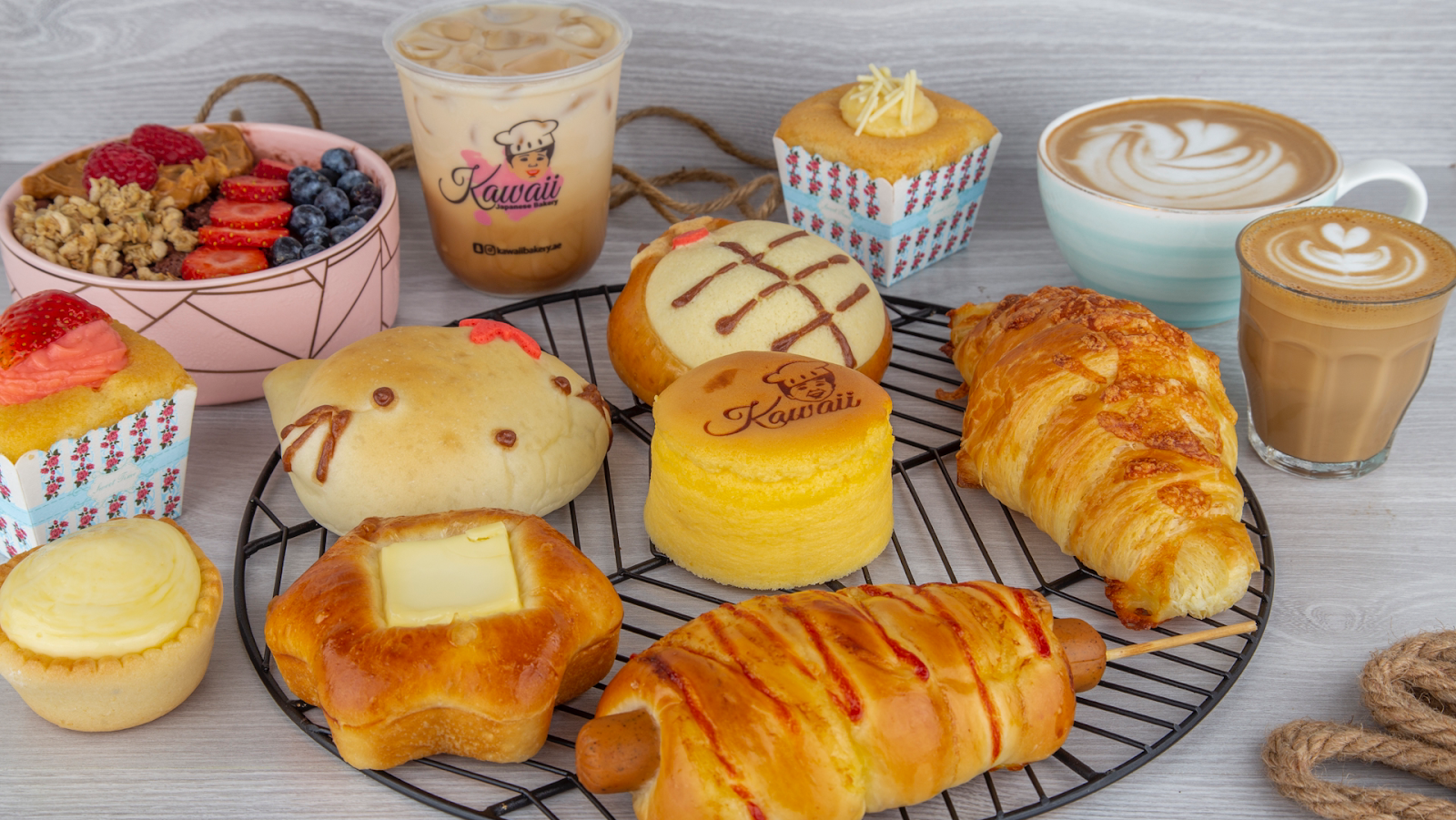 A spread of Kawaii signature pastries: character milk bun, logo-stamped fluffy cheesecake, cream horns, croissants and lattes