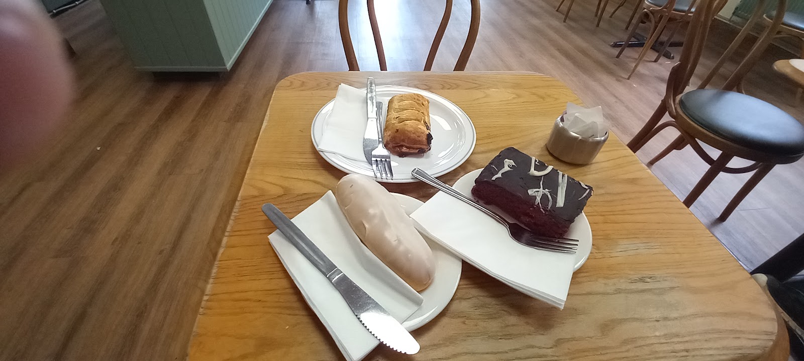 A pastry, chocolate slice and cream bun with coffee on a café table
