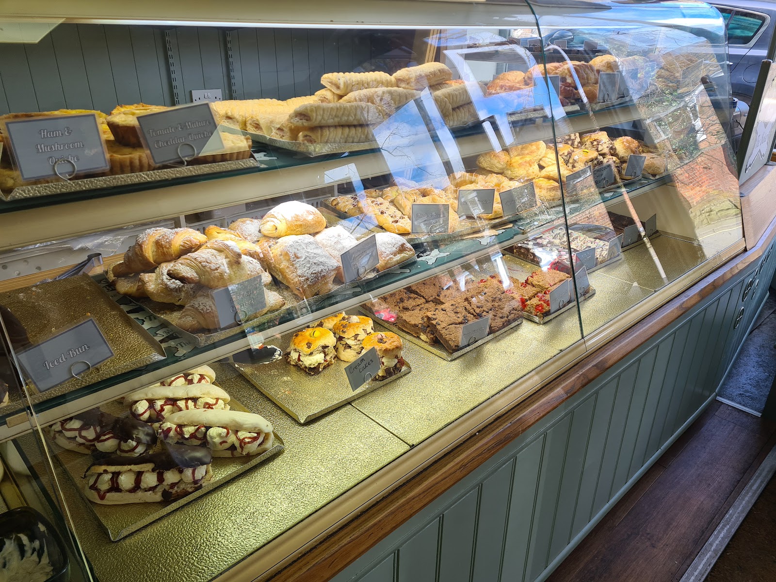 Glass display counter filled with pastries, sausage rolls, iced buns and traybakes