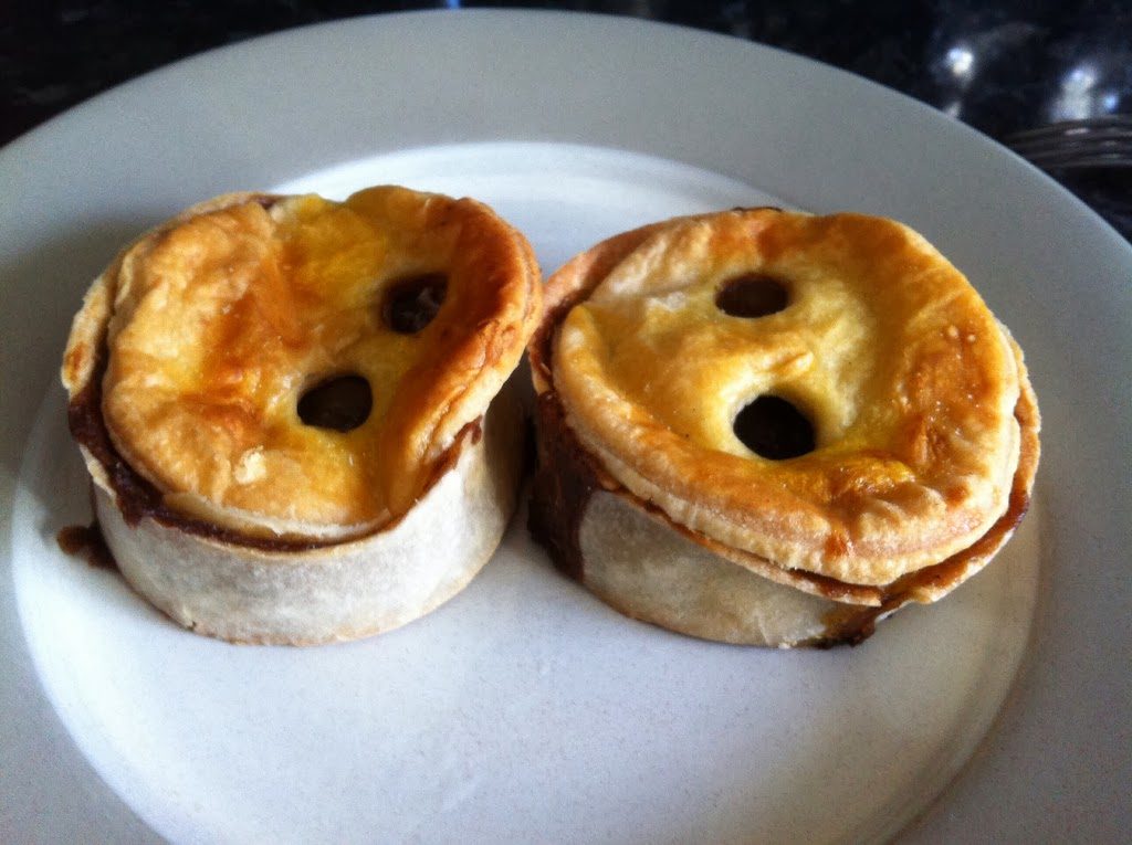 Two golden Paul Jones Bakery scotch pies on a plate, showing the twin steam-holes in the pastry lids
