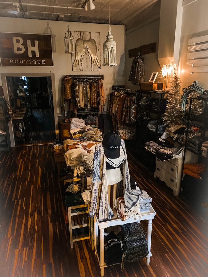 Inside Brave Hazel Boutique — a curated interior with the hand-painted BH Boutique wooden sign above racks of clothing and home goods