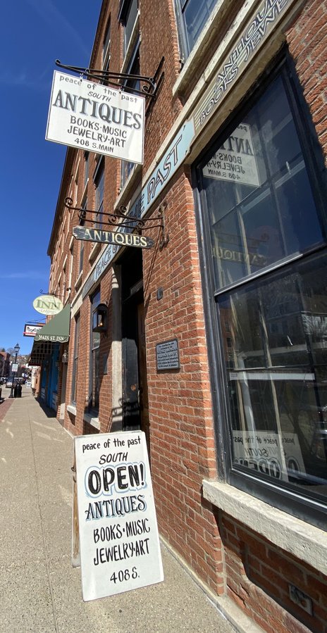 The exposed-brick Peace of the Past storefront on Main Street with its hanging wrought-iron Antiques sign and Open sandwich board