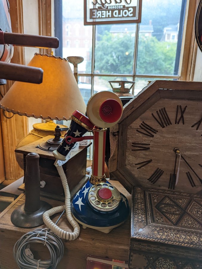 An antique candlestick telephone, a coffee grinder and a large handmade nail-numeral clock by the shop window