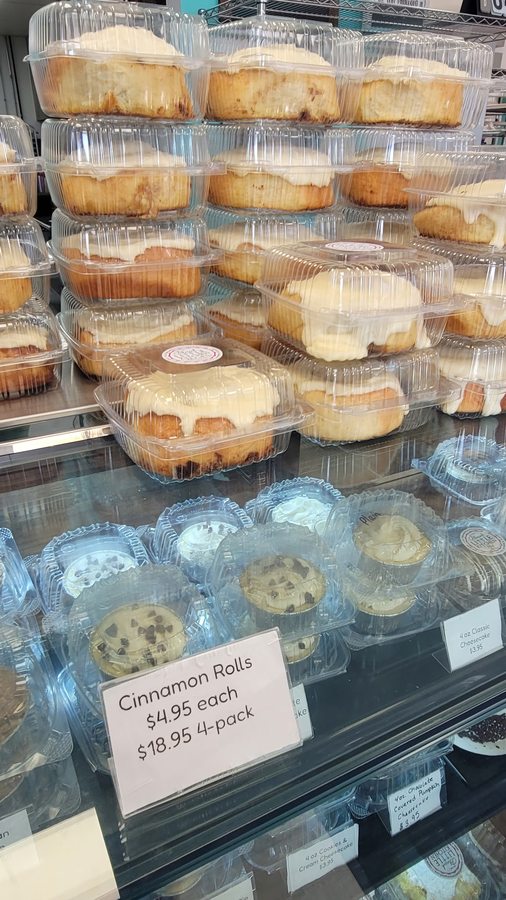 Blessed Little Kitchen display case with fresh cinnamon rolls topped in cream-cheese frosting and a hand-written price sign