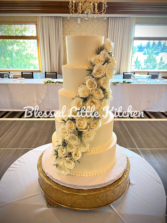 A five-tier white wedding cake with cascading fresh roses, made by Blessed Little Kitchen