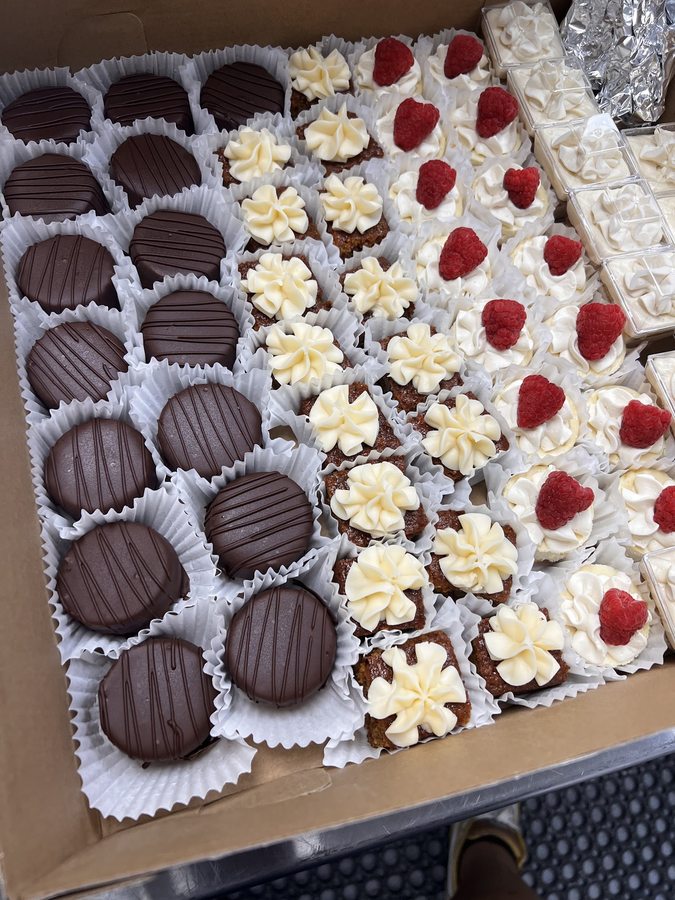 Catering tray of chocolate-dipped treats, frosted brownie bites and raspberry mini cheesecakes
