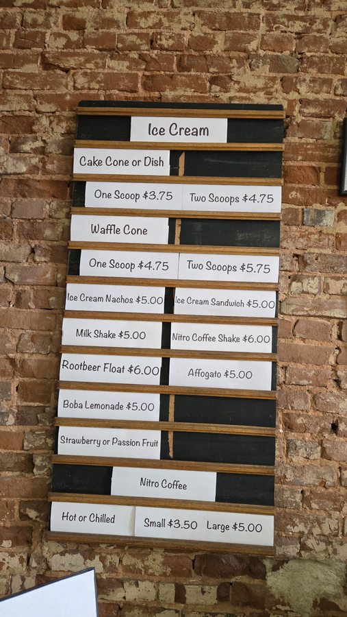 Sadie's in-shop ice cream menu board, listing cones, scoops, nachos, sandwiches, shakes and coffee with printed price strips.
