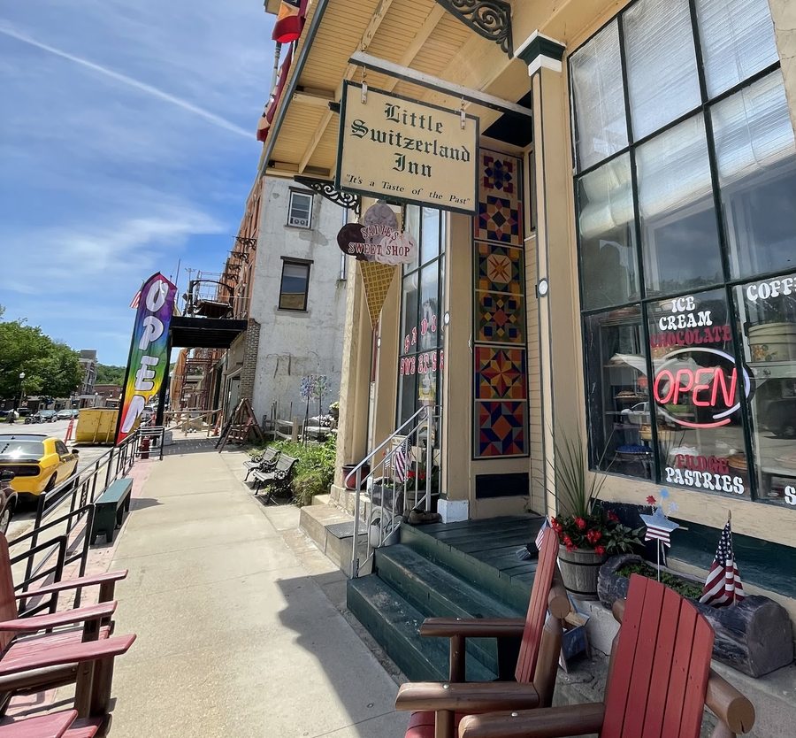 Sadie's Sweet Shop's storefront — cream clapboard with dark green trim, a hanging ice-cream-cone sign, red porch chairs, and a neon OPEN sign, in the historic Little Switzerland Inn building.