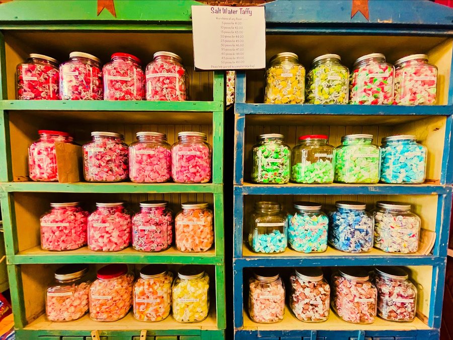 Shelves of glass jars packed with wrapped salt water taffy, with hand-written flavor labels.