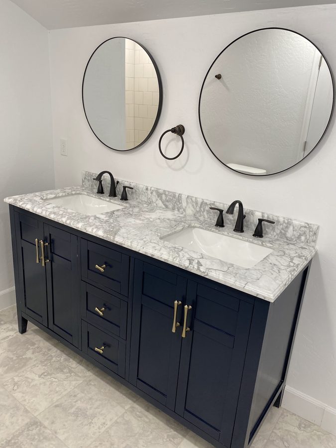 Finished bathroom remodel with a navy double vanity and marble countertop